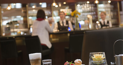 Latte macchiato and pastry at the café in Maritim Hotel Stuttgart with bar view in the background