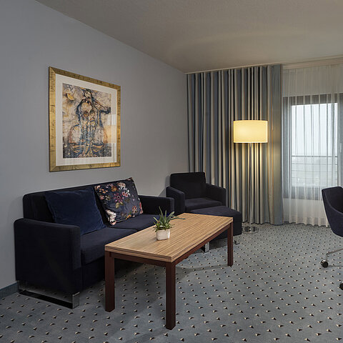 Junior suite at the Maritim Hotel Darmstadt with stylish decor, sofa, desk, TV, and large windows for ample daylight.