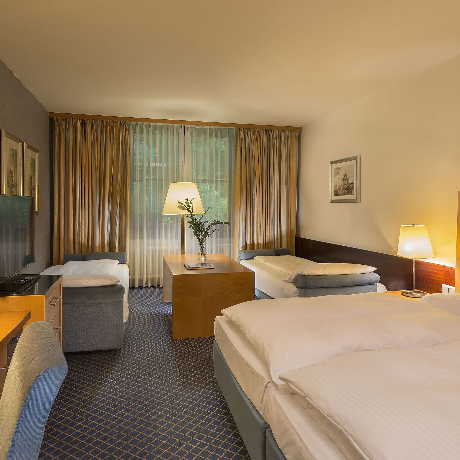 Spacious family room at Maritim Hotel Fulda with four beds, desk, and cozy atmosphere.