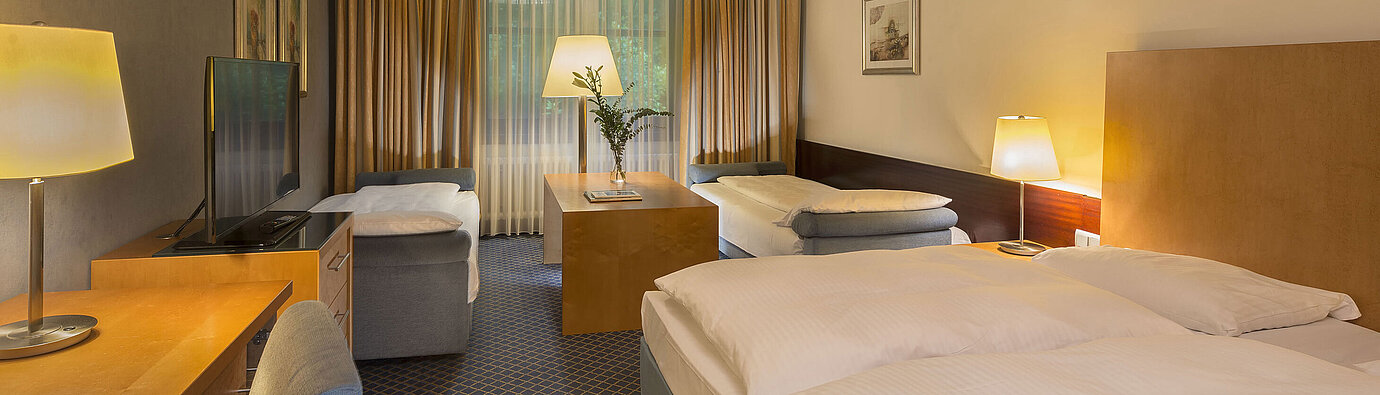 Spacious family room at Maritim Hotel Fulda with four beds, desk, and cozy atmosphere.