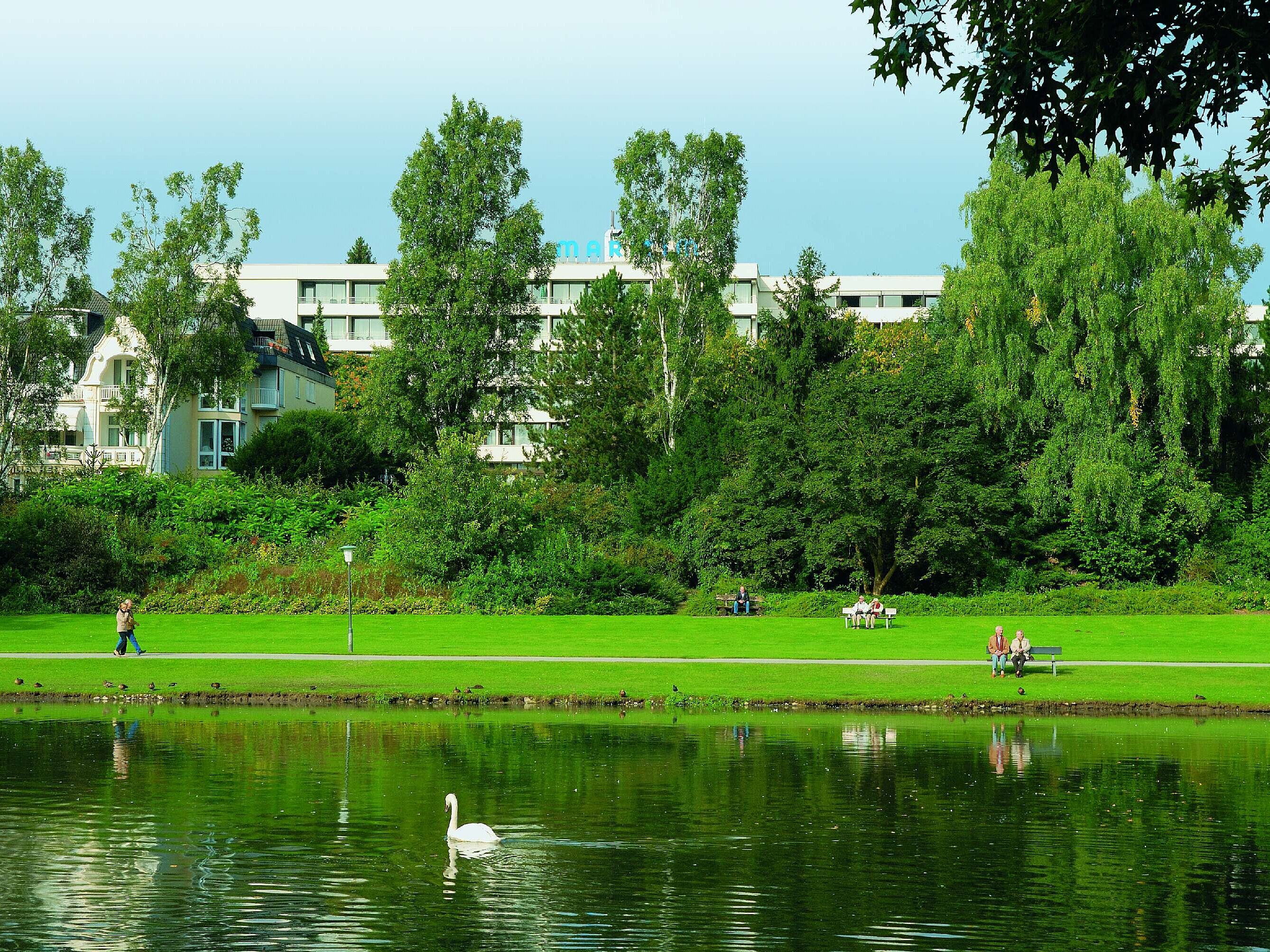 View of Maritim Hotel Bad Salzuflen behind the green spa park with lake and swan