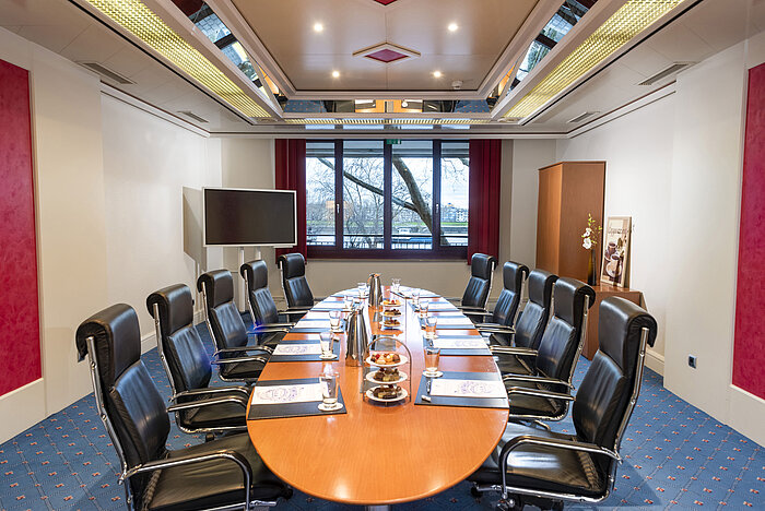 The Boardroom at Maritim Cologne, featuring an oval conference table, leather chairs, and conference materials.