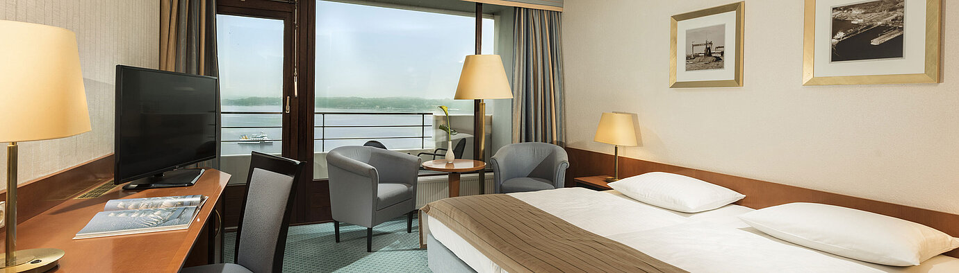 Superior room at the Maritim Hotel Kiel with desk, seating area, large double bed and balcony overlooking the fjord.