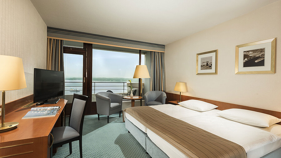 Superior room at the Maritim Hotel Kiel with desk, seating area, large double bed and balcony overlooking the fjord.
