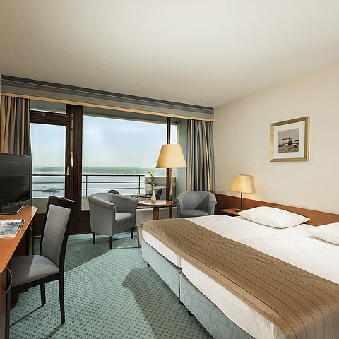 Superior room at the Maritim Hotel Kiel with desk, seating area, large double bed and balcony overlooking the fjord.