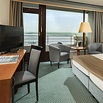 Superior room at the Maritim Hotel Kiel with desk, seating area, large double bed and balcony overlooking the fjord.