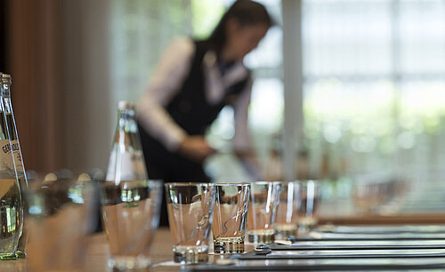 Staff member preparing conference table with glasses and water bottles for meeting