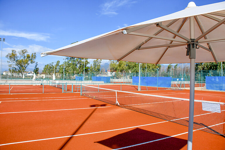 Sunshade at the red tennis court of Maritim Resort Calabria invites to sporty relaxation outdoors