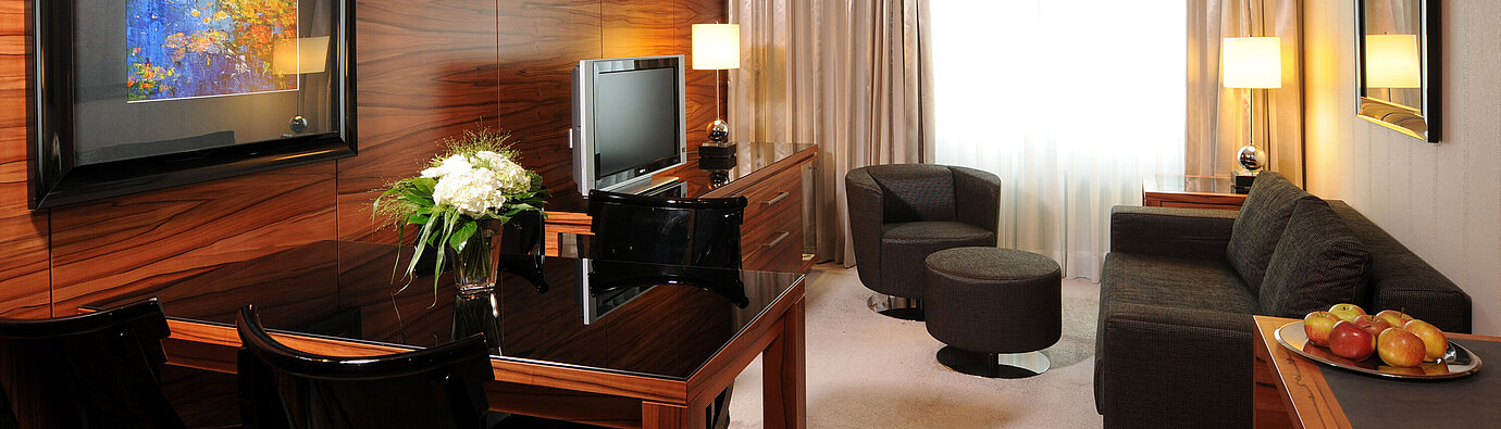 Bright living space with sofa, armchair, TV and desk at Maritim Hotel Munich