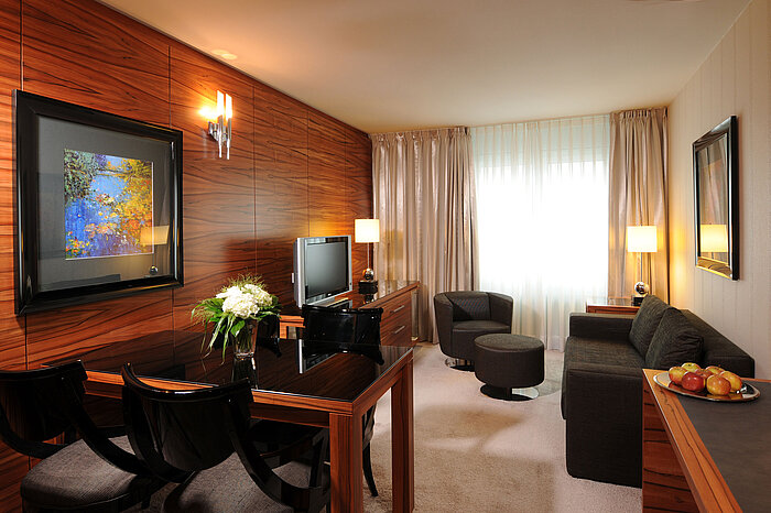 Bright living space with sofa, armchair, TV and desk at Maritim Hotel Munich