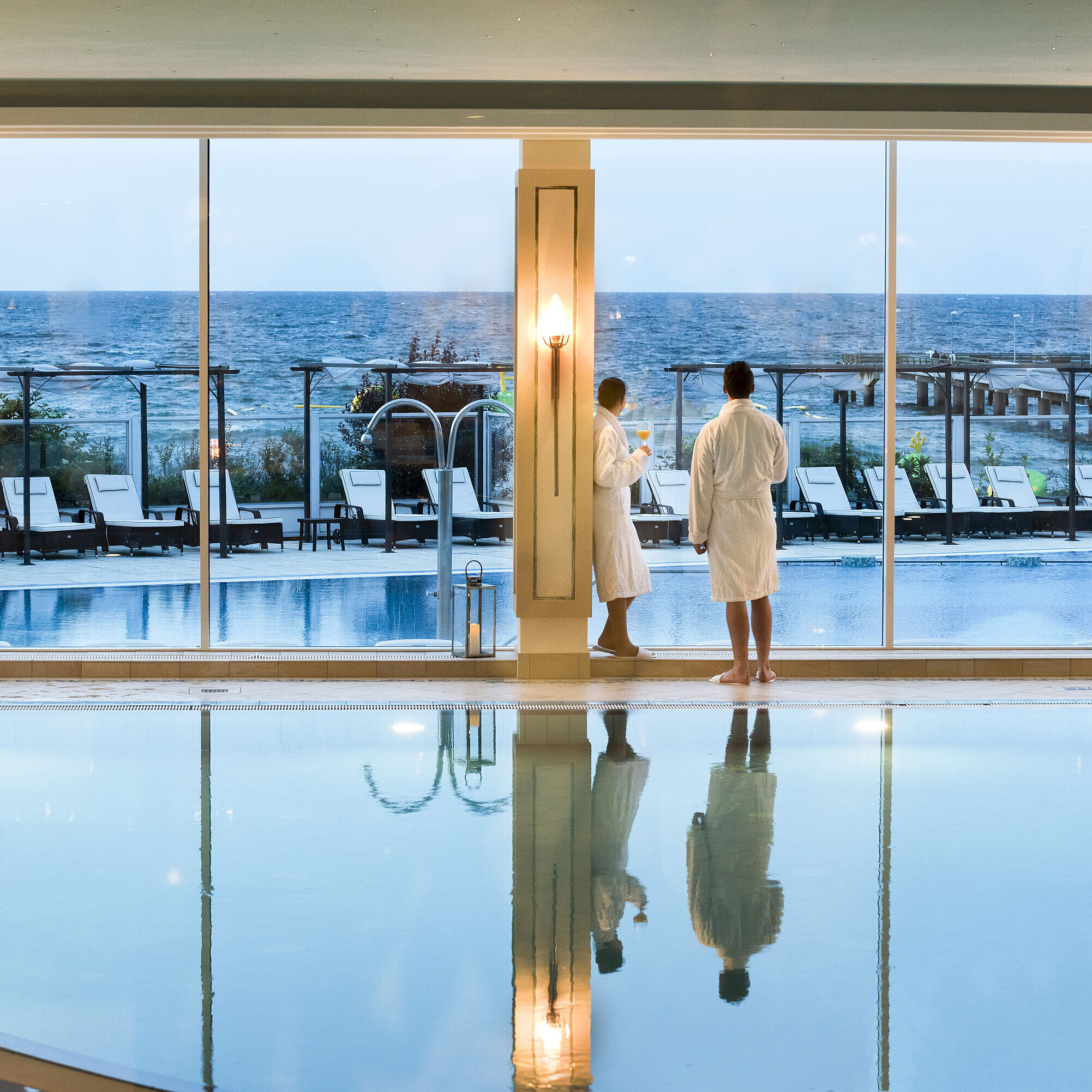 Indoor pool with sea view at Maritim Seehotel Timmendorfer Strand, two guests in bathrobes by the window.