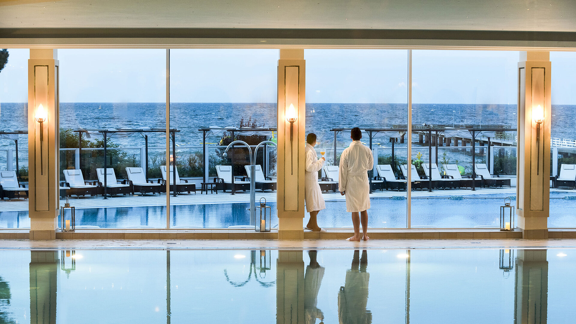 Indoor pool with sea view at Maritim Seehotel Timmendorfer Strand, two guests in bathrobes by the window.
