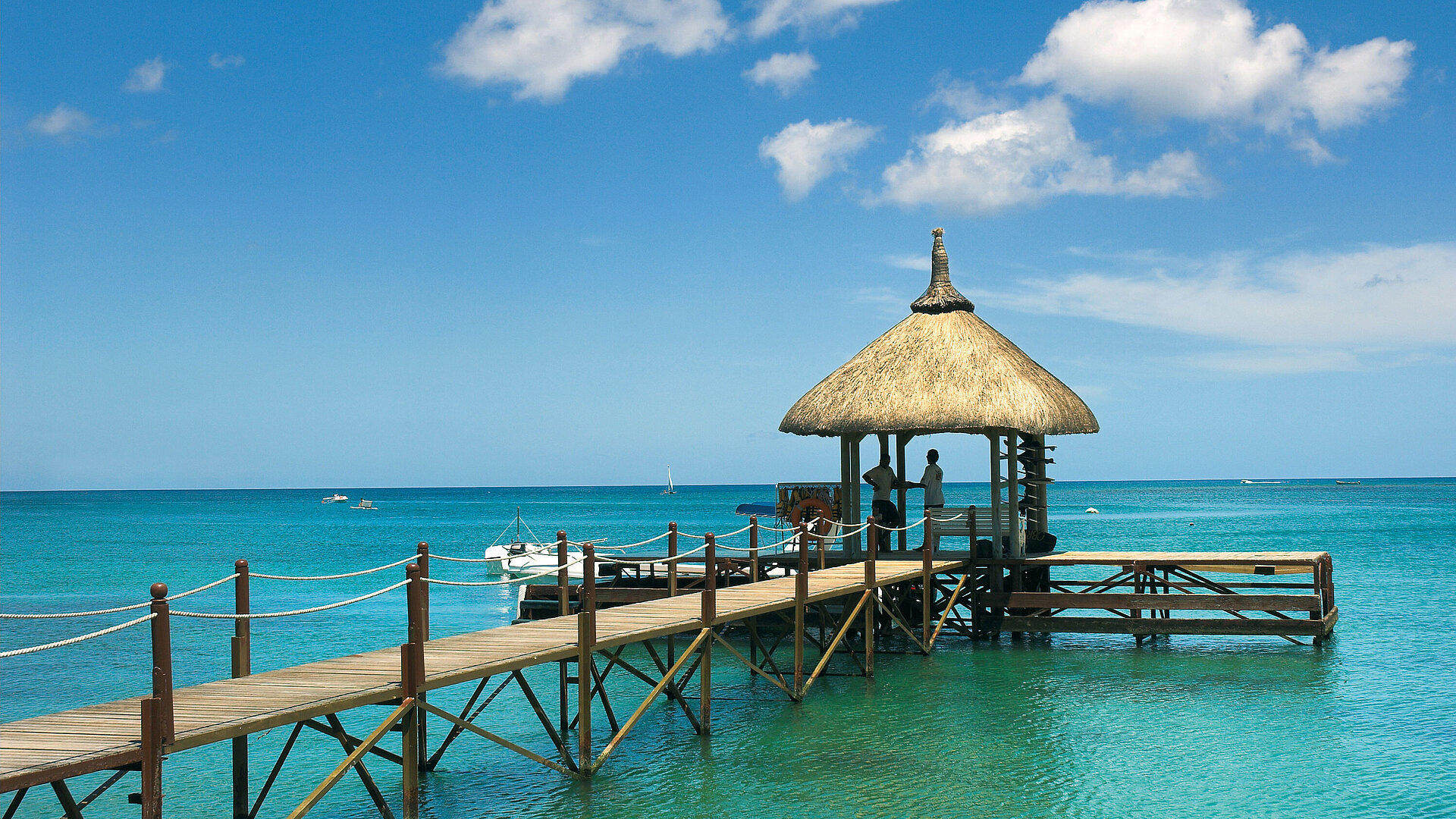 Wooden pier with pavilion over clear seawater, boats in the background