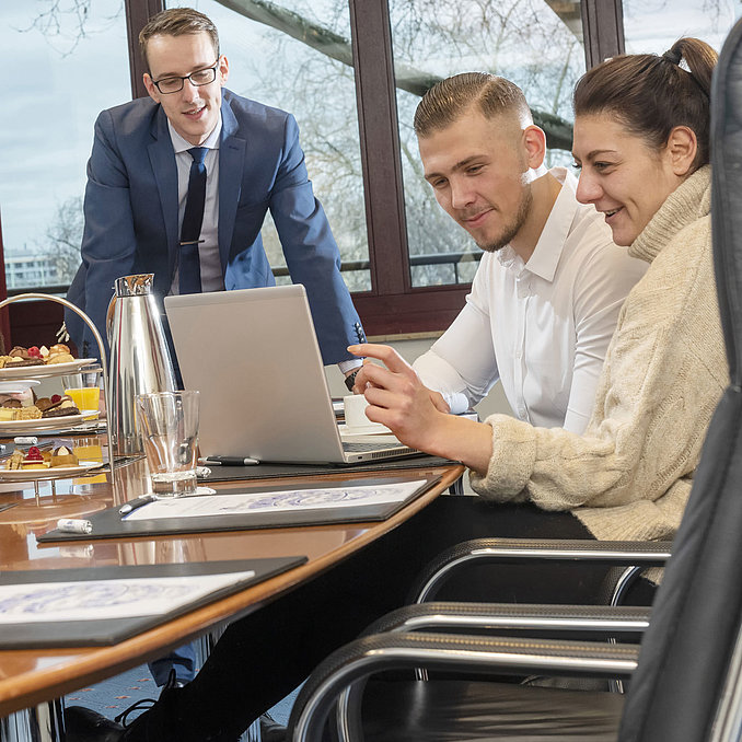 Team in a meeting in the Boardroom at Maritim Cologne, with coffee and snacks on the table, working on a laptop.