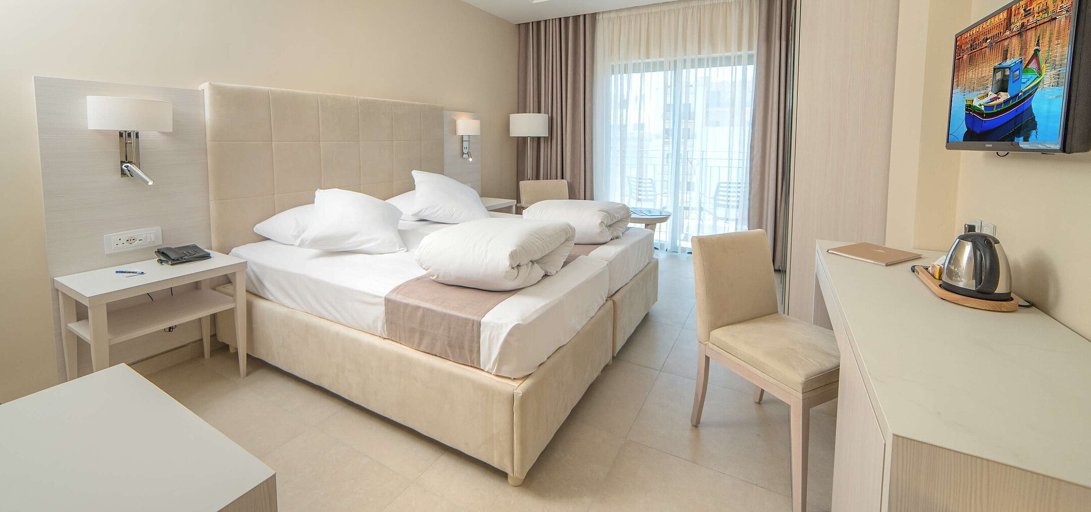 Modern double room with comfortable beds, desk, TV and balcony with natural daylight