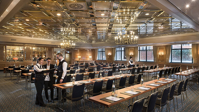 Two staff members preparing a conference room with row seating at Maritim Hotel Stuttgart