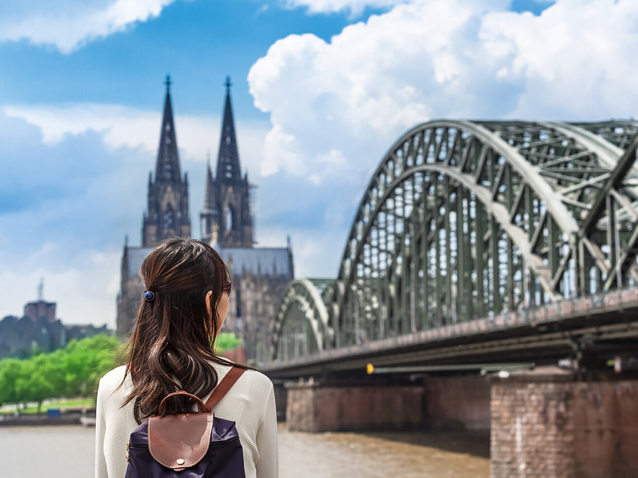 Woman with backpack looking at Cologne Cathedral and Hohenzollern Bridge by the Rhine