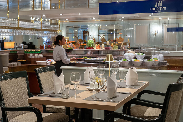 Restaurant area with set table, buffet station in the background and a staff member at Maritim Hotel.