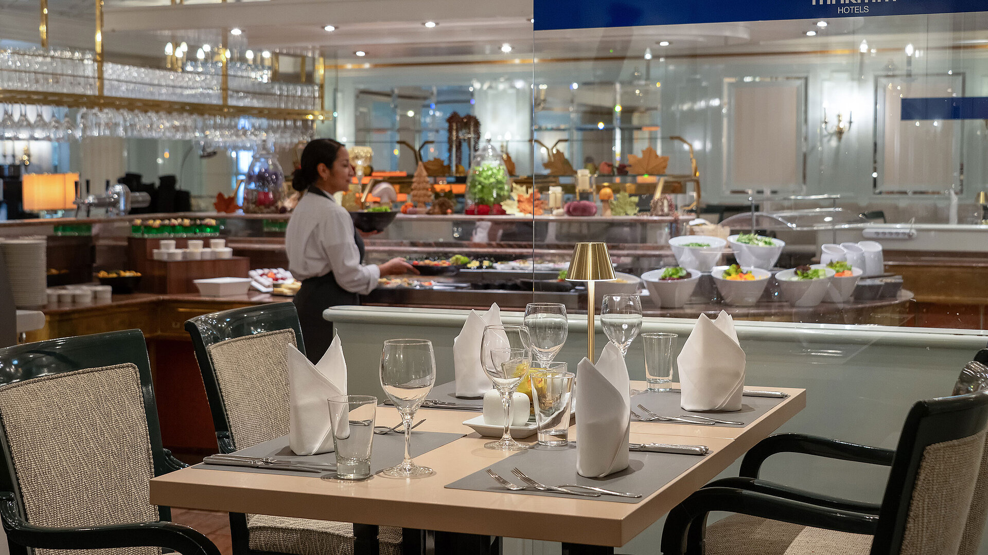 Restaurant area with set table, buffet station in the background and a staff member at Maritim Hotel.