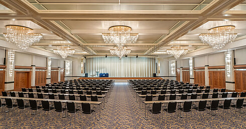 Salle Fürst-von-Metternich avec grande scène, rangées de sièges, lustres élégants et ambiance lumineuse.