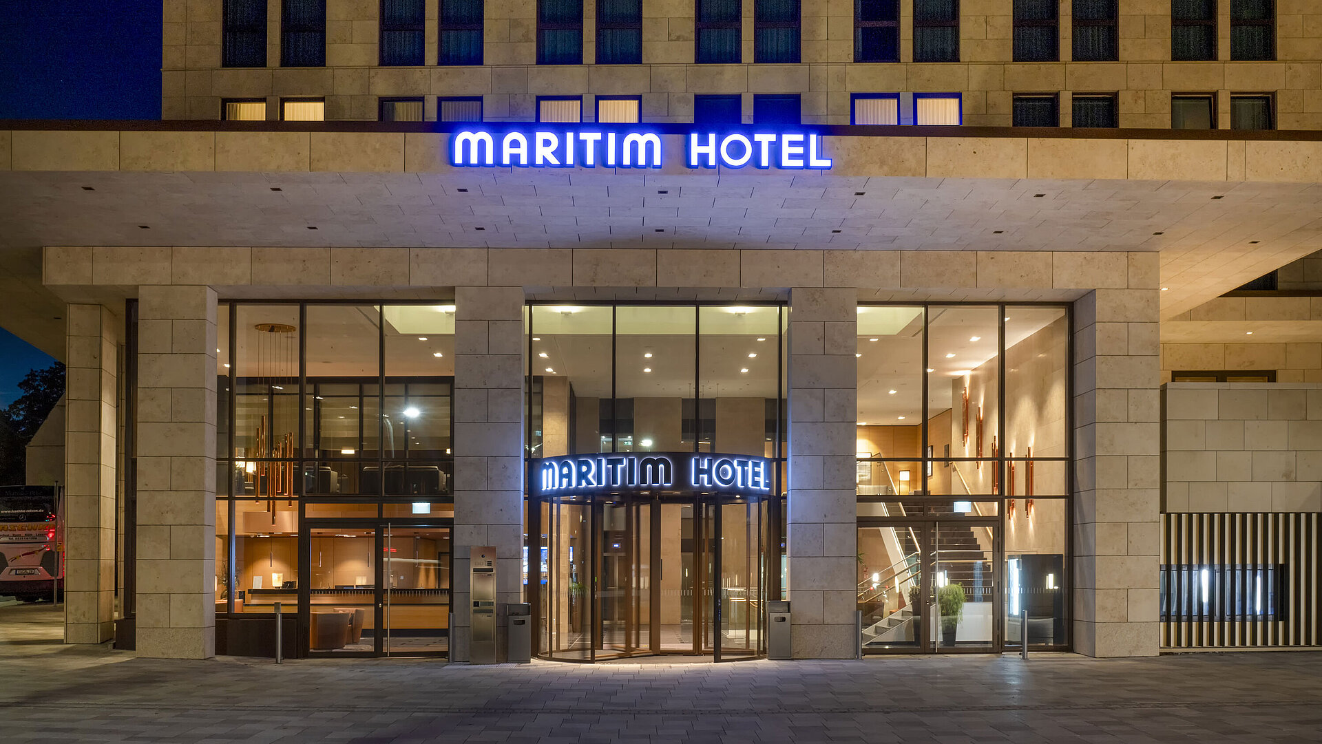 Illuminated entrance of Maritim Hotel Ingolstadt with modern glass facade at night.