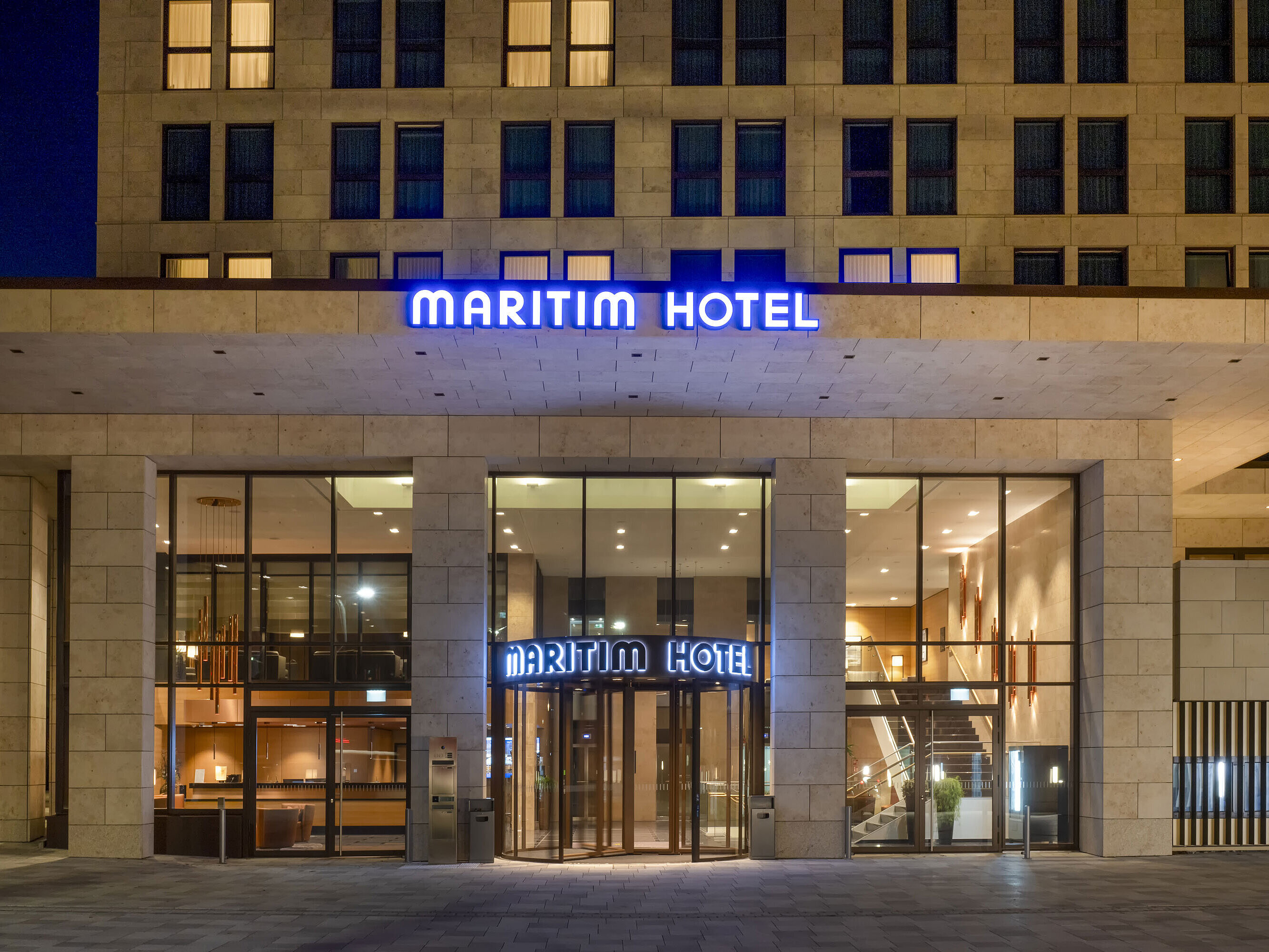 Illuminated entrance of Maritim Hotel Ingolstadt with modern glass facade at night.