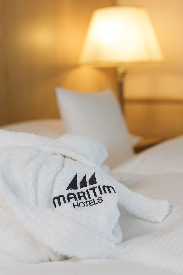 Soft bathrobe with Maritim Hotels logo on a freshly made bed in the hotel room