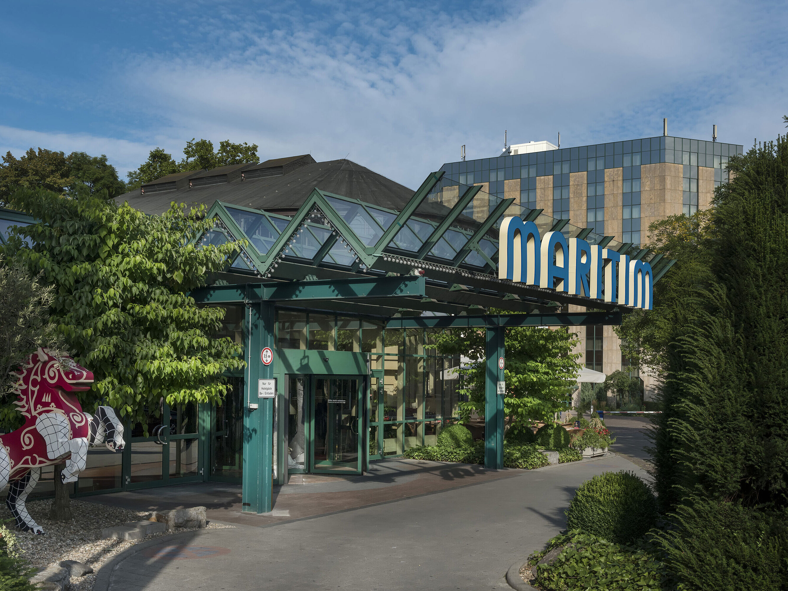 Main entrance of Maritim Hotel Stuttgart with glass roof, green facade and Maritim logo