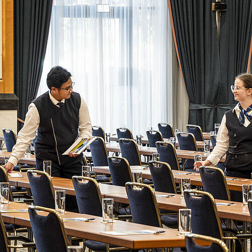 Staff members at the Maritim Hotel Magdeburg preparing the hall with glasses and materials on the tables.