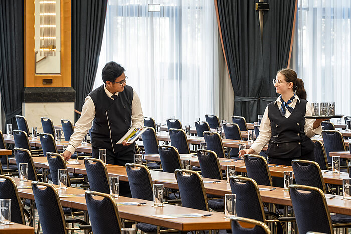 Staff members at the Maritim Hotel Magdeburg preparing the hall with glasses and materials on the tables.