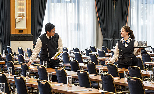 Staff members at the Maritim Hotel Magdeburg preparing the hall with glasses and materials on the tables.