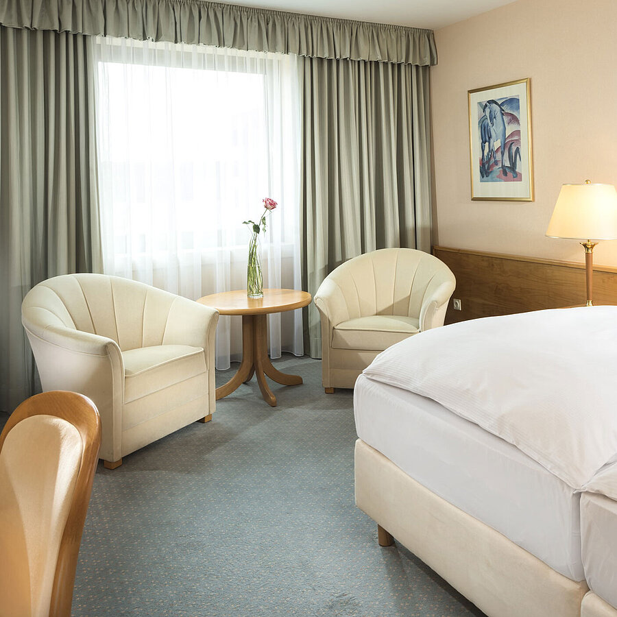 Bright hotel room with two beds, seating area and large window at Maritim Hotel Magdeburg