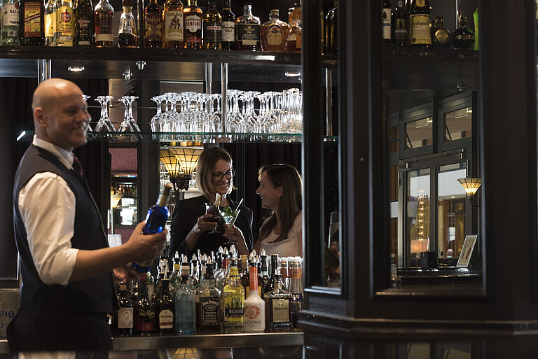 Happy guests enjoying cocktails at the bar of Maritim Hotel Dresden, served by a friendly bartender.