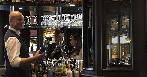 Happy guests enjoying cocktails at the bar of Maritim Hotel Dresden, served by a friendly bartender.