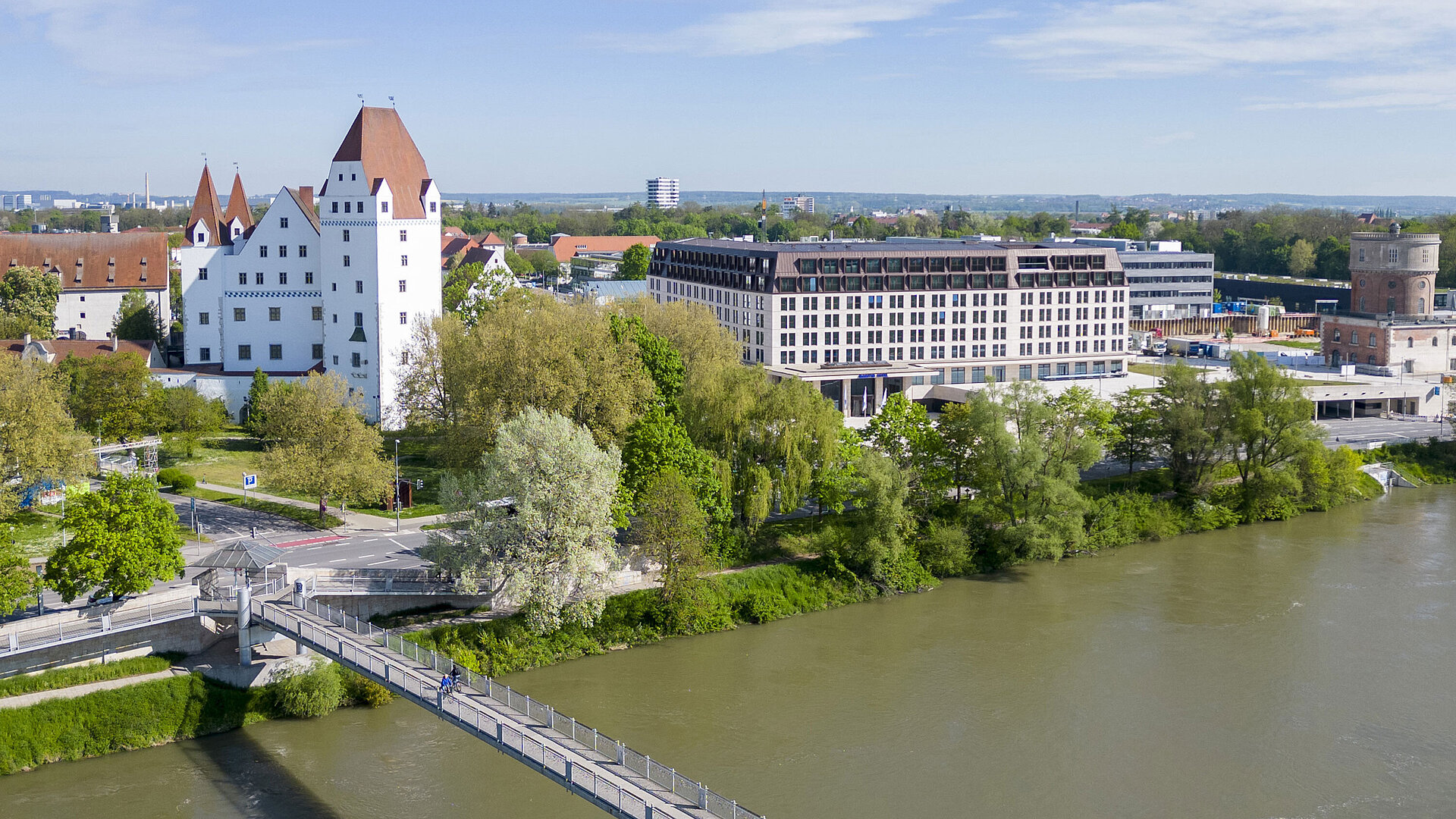 Aerial view of Maritim Hotel Ingolstadt overlooking the Danube, a pedestrian bridge, and the historic castle.