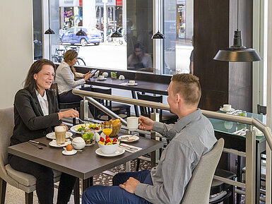 Guests enjoying a hearty breakfast at Maritim proArte Hotel Berlin, surrounded by modern decor and large windows.