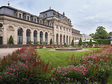 The historic Orangerie in Fulda with a baroque facade, staircase, and blooming garden in the foreground.