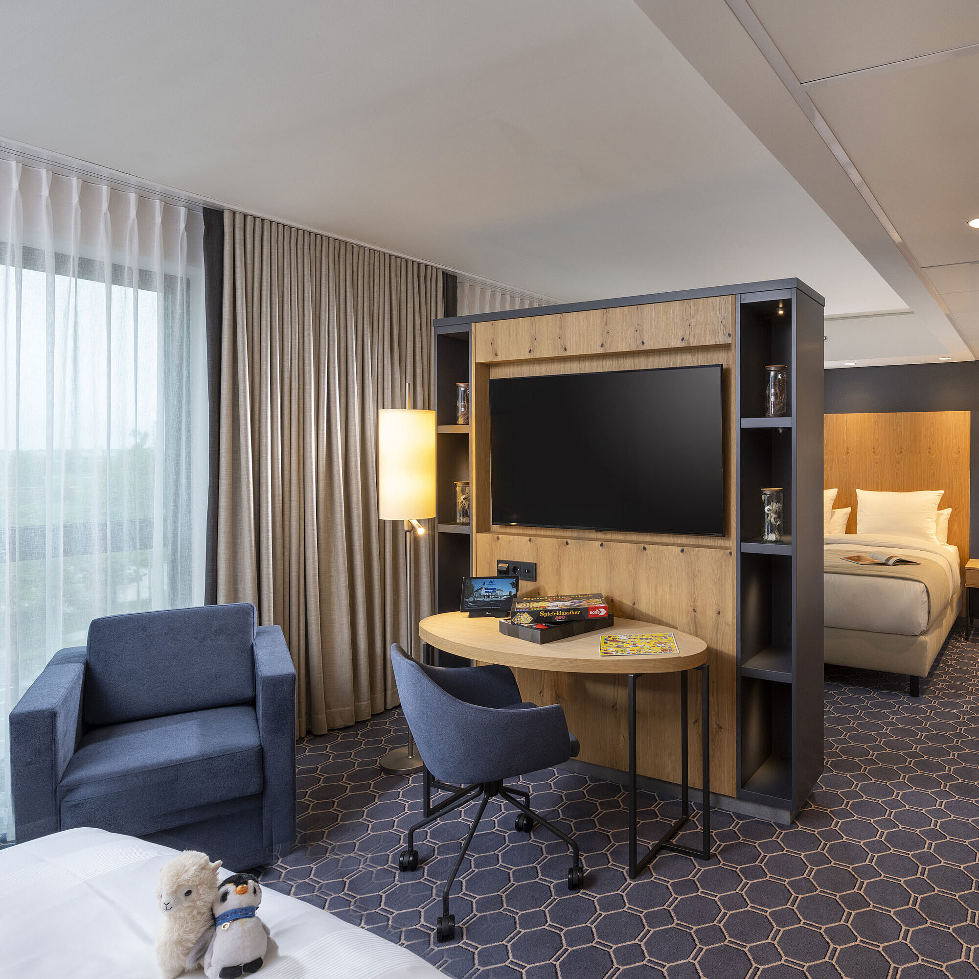 Bright room at Maritim Hotel Ingolstadt with seating area, desk, large TV, and view of the green surroundings.