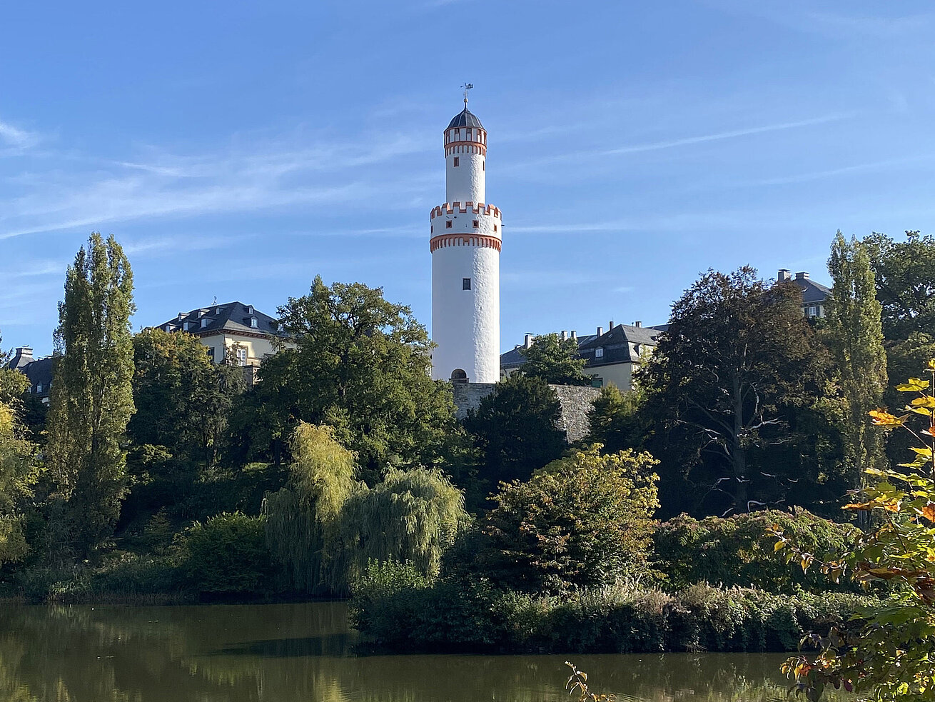 White tower in Bad Homburg with blue sky and surrounded by green nature.