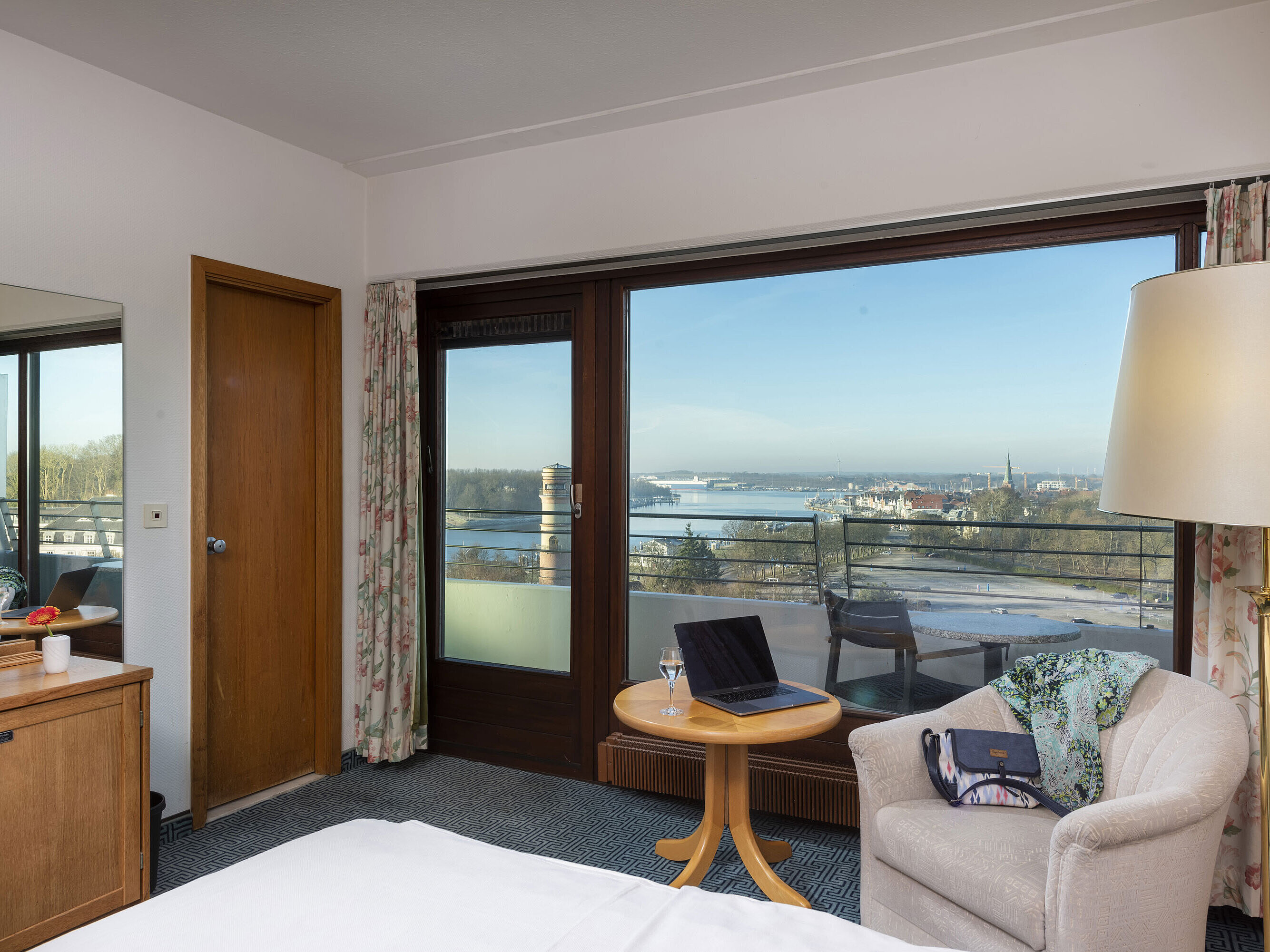 Bright hotel room with balcony, desk and view of the Trave River and Lübeck Bay