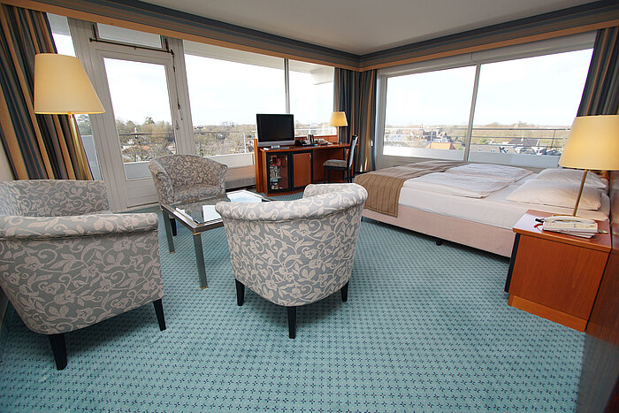 Comfort room at the Maritim Hotel Kiel, with seating area, desk, double bed and large windows overlooking the city.