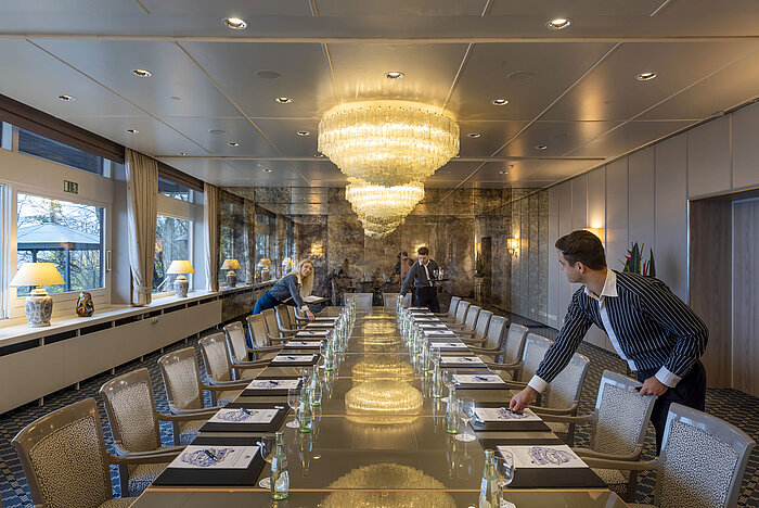 Salon Oslo in the Maritim Hotel Kiel, elegant conference room with chandeliers and a long row of tables, staff setting up the room.