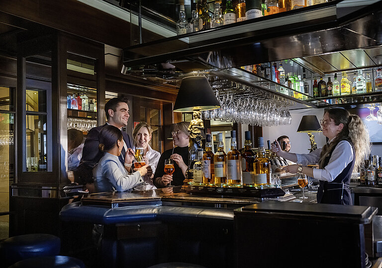 Guests enjoying cocktails and great vibes at the bar of Maritim Hotel Darmstadt. Friendly bar staff serving drinks.