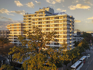 Exterior view of the Maritim Hotel Darmstadt at sunset with modern architecture and trees in the foreground.
