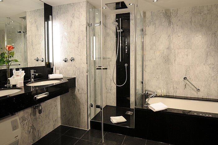 Modern bathroom with marble tiles, shower, bathtub and double sink at Maritim Hotel Munich