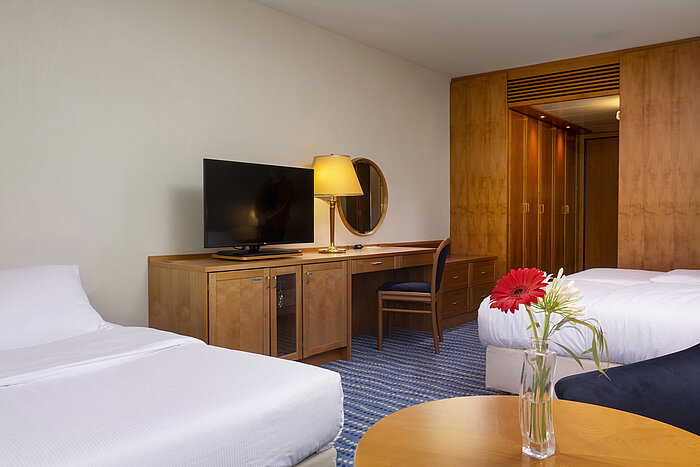 Classic family room with two beds, desk, flat-screen TV, and vase with fresh flowers on the table.