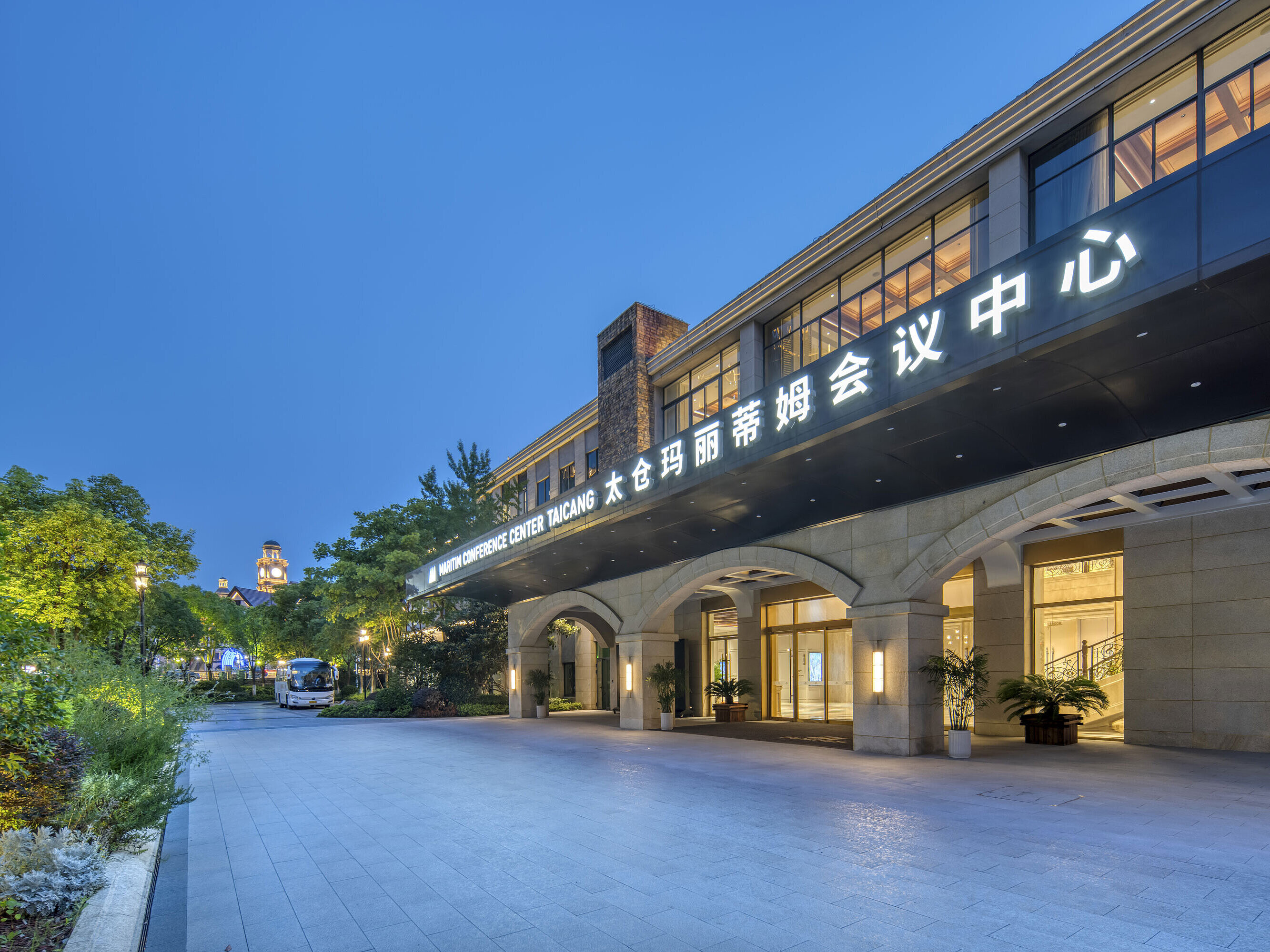 Illuminated entrance of the Maritim Conference Center Taicang at dusk, framed by greenery and modern design