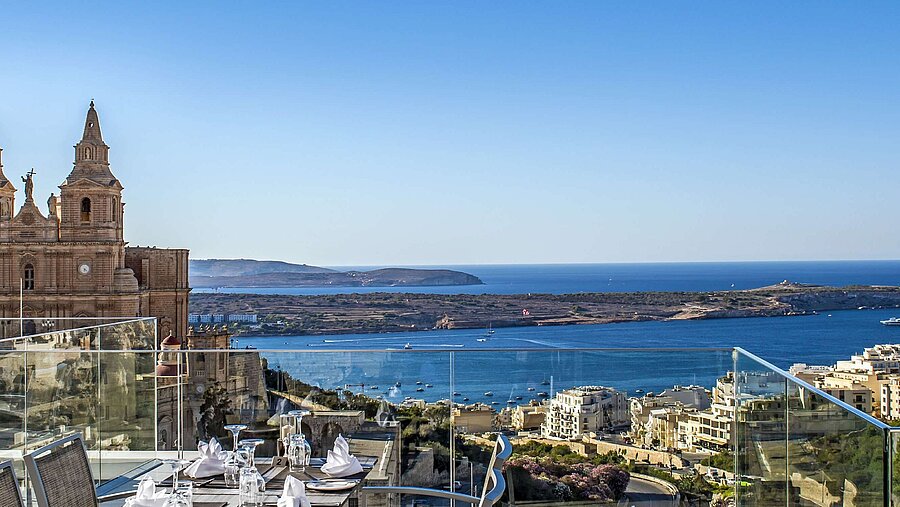 Rooftop restaurant with set tables, views of church, coastline and blue Mediterranean Sea