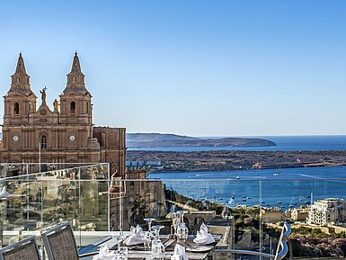 Rooftop restaurant with set tables, views of church, coastline and blue Mediterranean Sea