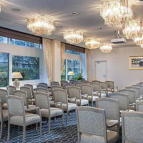 Salon Helsinki in the Maritim Hotel Kiel, conference room with rows of chairs, chandeliers and large windows with a view of the greenery.